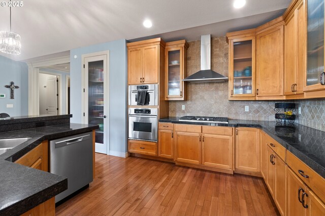 kitchen featuring backsplash, pendant lighting, wood finished floors, wall chimney range hood, and appliances with stainless steel finishes