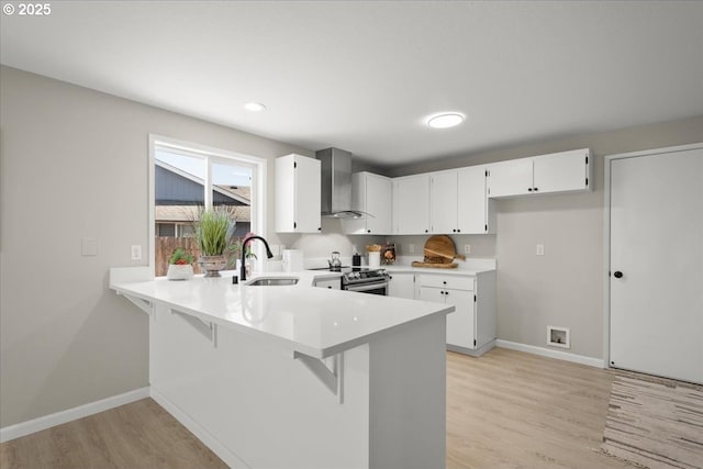 kitchen featuring wall chimney range hood, a sink, stainless steel range with electric cooktop, a peninsula, and light wood-style floors