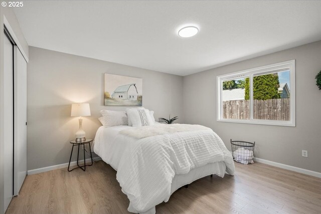 bedroom with light wood-type flooring, a closet, and baseboards