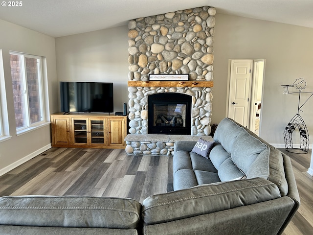 living area with baseboards, vaulted ceiling, wood finished floors, and a stone fireplace