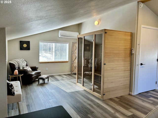 sitting room with vaulted ceiling, a textured ceiling, a wall mounted air conditioner, and wood finished floors