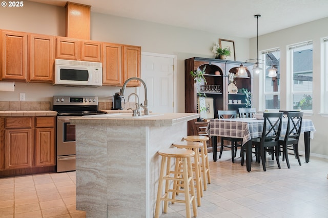 311 W Jadon Dr, Lebanon, OR 97355 - kitchen with white microwave, stainless steel electric stove, a sink, a kitchen bar, and a kitchen island with sink