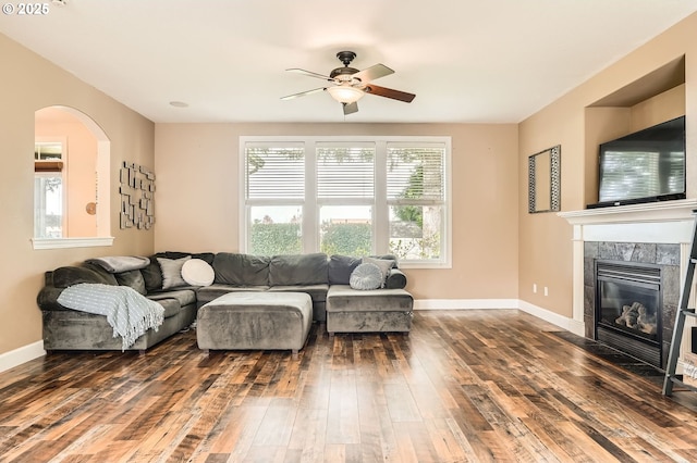 living room with arched walkways, hardwood / wood-style flooring, a fireplace, baseboards, and a ceiling fan