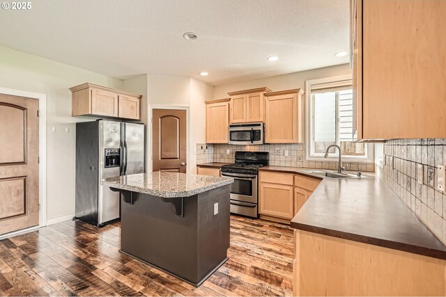 kitchen with tasteful backsplash, a sink, appliances with stainless steel finishes, a center island, and light brown cabinetry