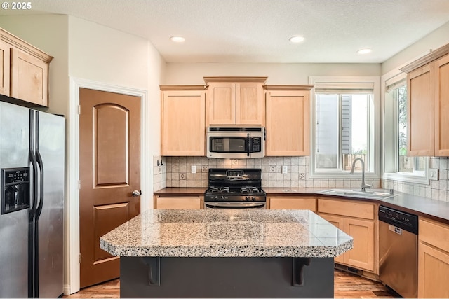 kitchen with appliances with stainless steel finishes, light wood finished floors, light brown cabinetry, and a sink