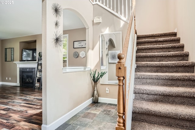 stairs featuring arched walkways, a tiled fireplace, and baseboards