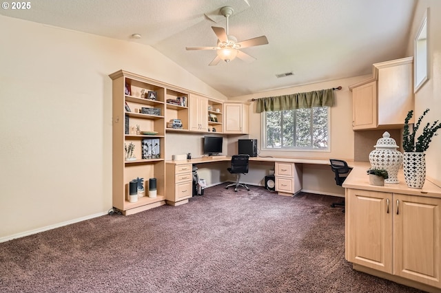 office space with lofted ceiling, dark carpet, built in desk, visible vents, and ceiling fan