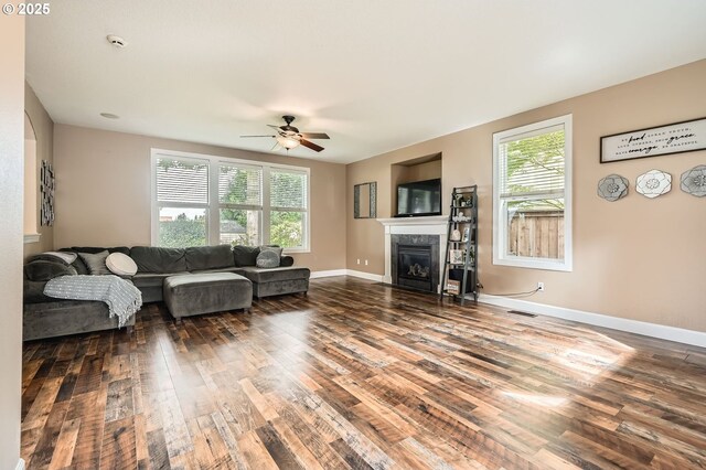 living area featuring ceiling fan, visible vents, baseboards, a glass covered fireplace, and wood finished floors