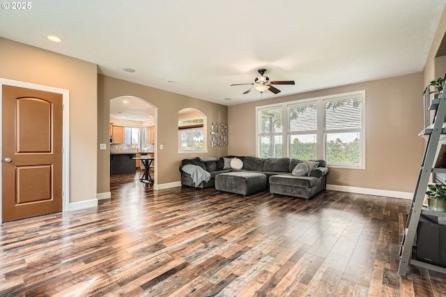 living room featuring baseboards, wood finished floors, a ceiling fan, and a wealth of natural light