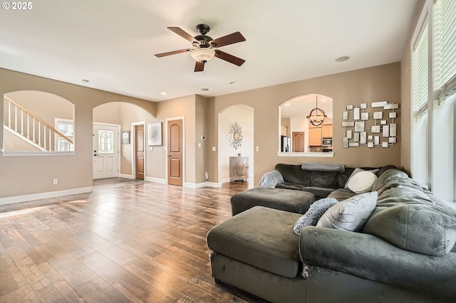 living area with arched walkways, a wealth of natural light, wood finished floors, and ceiling fan