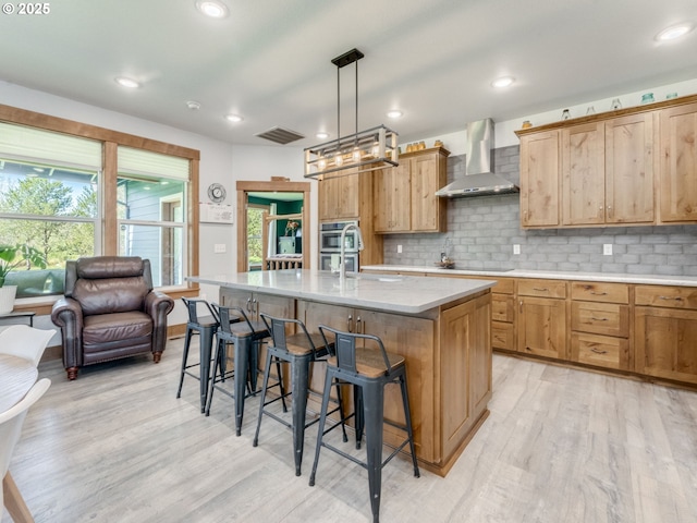 kitchen featuring light wood-type flooring, wall chimney exhaust hood, a kitchen breakfast bar, and a healthy amount of sunlight