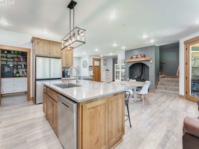 kitchen featuring light brown cabinets, a sink, open floor plan, light wood-style flooring, and appliances with stainless steel finishes