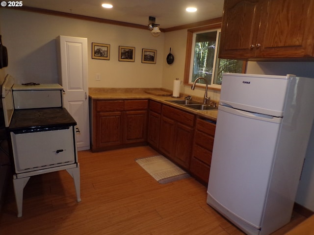 kitchen featuring brown cabinets, light wood-style floors, freestanding refrigerator, ornamental molding, and a sink