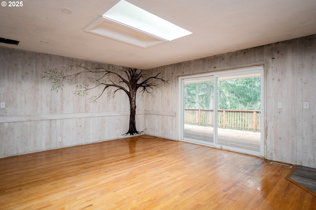 unfurnished room featuring wooden walls, light hardwood / wood-style floors, and a skylight