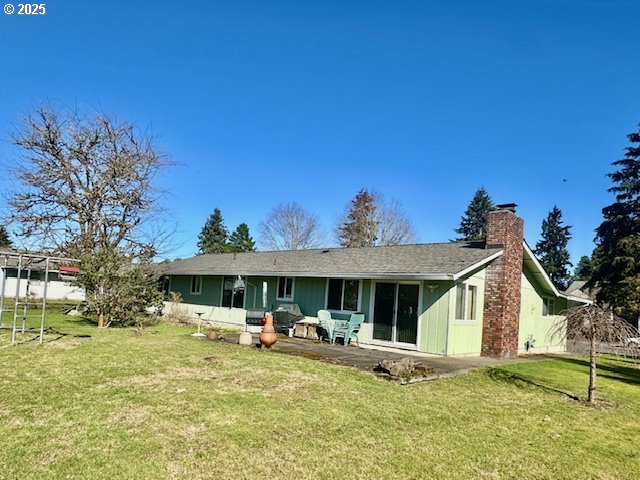 rear view of property with a chimney, a patio area, and a lawn