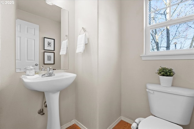 half bath featuring wood finished floors, toilet, and baseboards