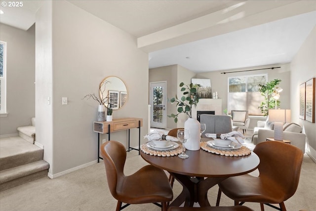 dining space featuring light carpet, stairs, a fireplace, and baseboards