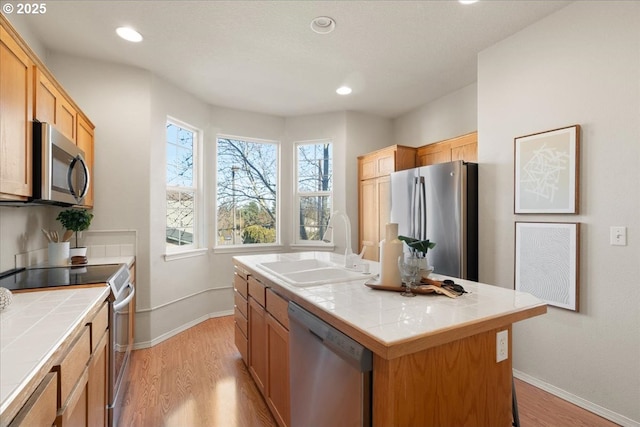 kitchen with appliances with stainless steel finishes, light wood-style flooring, a sink, and tile counters