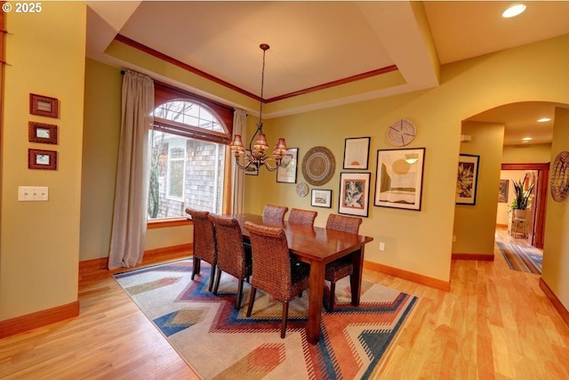 dining space with ornamental molding, light wood-type flooring, an inviting chandelier, and a tray ceiling