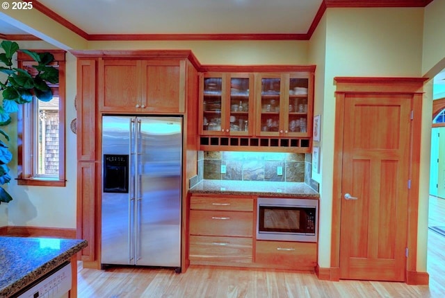 kitchen featuring built in appliances, light wood-type flooring, ornamental molding, stone countertops, and backsplash