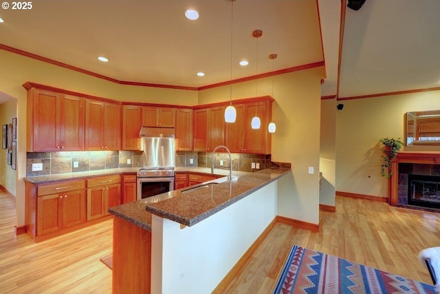 kitchen with a tile fireplace, stainless steel stove, kitchen peninsula, pendant lighting, and a kitchen bar