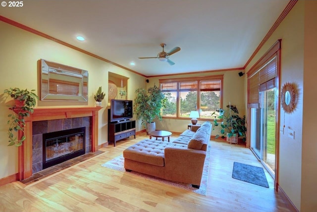 living room featuring ceiling fan, light wood-type flooring, ornamental molding, and a tiled fireplace