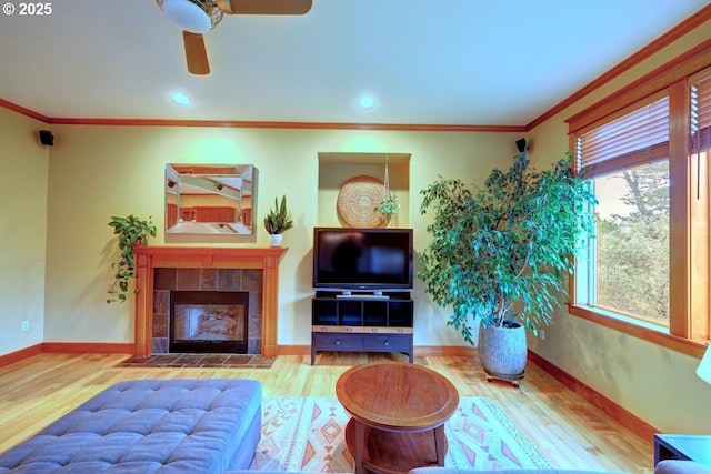 living room featuring ceiling fan, a tiled fireplace, ornamental molding, and wood-type flooring