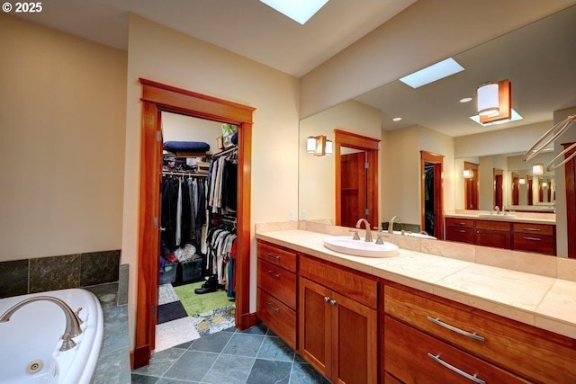 bathroom featuring a relaxing tiled tub, a skylight, and vanity