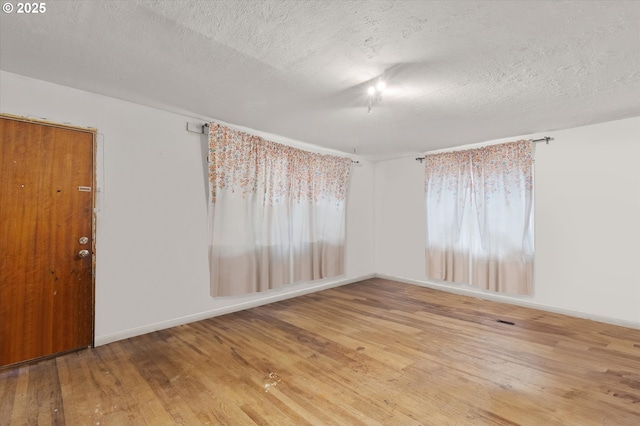 empty room featuring a textured ceiling, baseboards, and hardwood / wood-style flooring