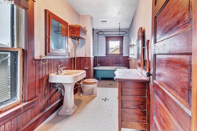 bathroom with toilet, tile patterned flooring, wooden walls, and a bathtub