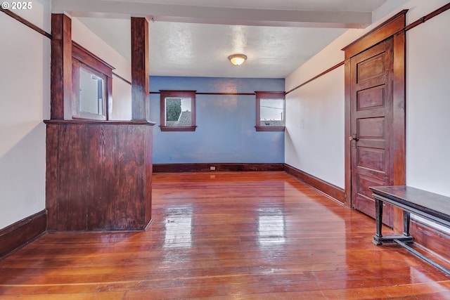 empty room with beam ceiling and hardwood / wood-style floors