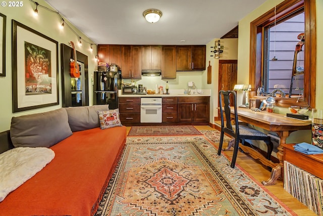 kitchen featuring black refrigerator, light wood-type flooring, white oven, and sink