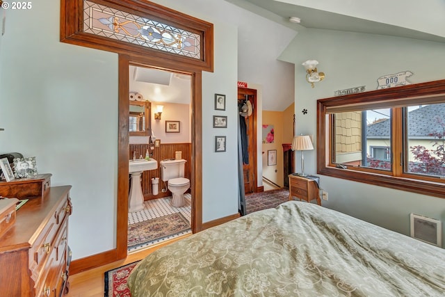 bedroom with lofted ceiling, light wood-type flooring, and connected bathroom