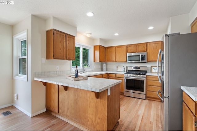 11442 SW Woodlee Heights Ct, Portland, OR 97219 - kitchen featuring stainless steel appliances, a peninsula, light wood-type flooring, a breakfast bar area, and recessed lighting