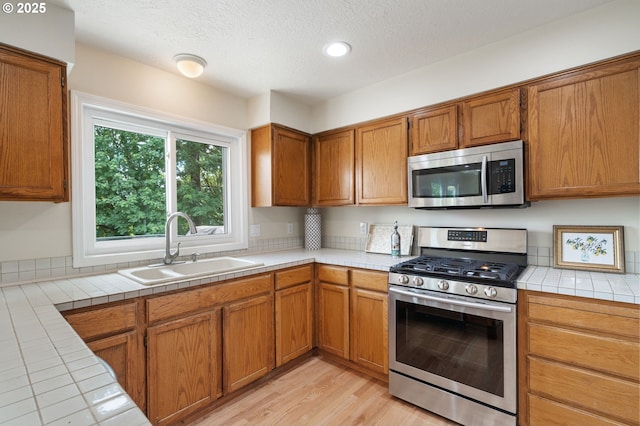 11442 SW Woodlee Heights Ct, Portland, OR 97219 - kitchen with appliances with stainless steel finishes, tile countertops, brown cabinets, a textured ceiling, and light wood-style floors