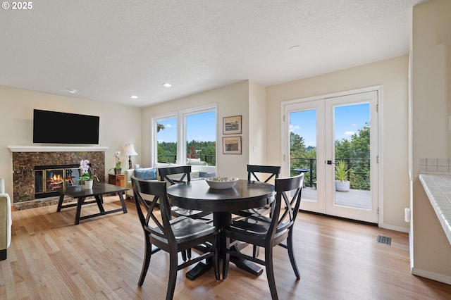 11442 SW Woodlee Heights Ct, Portland, OR 97219 - dining space with french doors, light wood-style floors, a fireplace, a textured ceiling, and recessed lighting