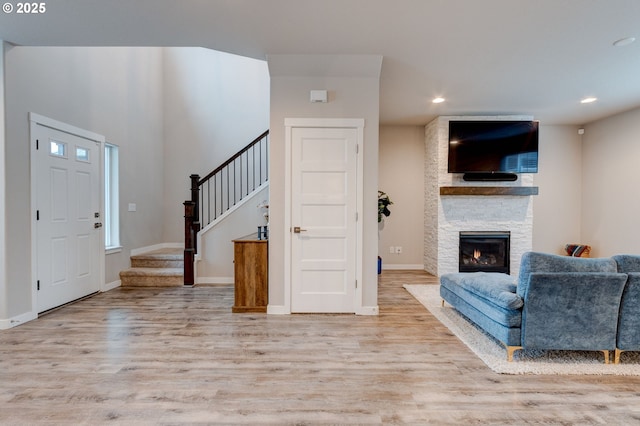 entryway with recessed lighting, light wood-style flooring, stairway, a stone fireplace, and baseboards