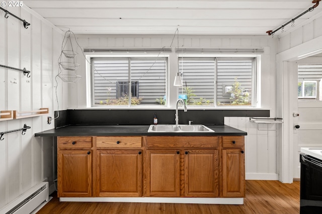kitchen featuring baseboard heating, a sink, light wood-style flooring, and dark countertops