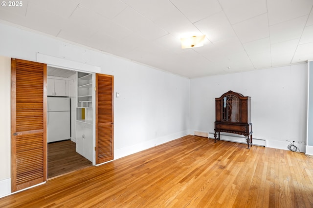 spare room featuring baseboard heating, light wood finished floors, and baseboards