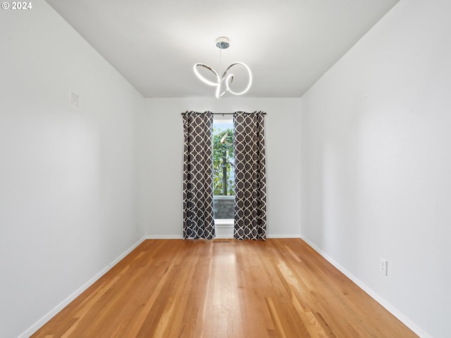 spare room featuring a chandelier and light wood-type flooring