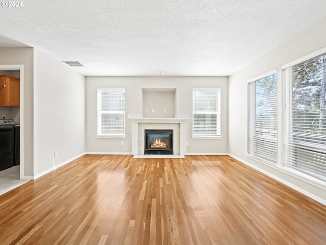 unfurnished living room featuring washer / dryer, light hardwood / wood-style flooring, plenty of natural light, and a tiled fireplace