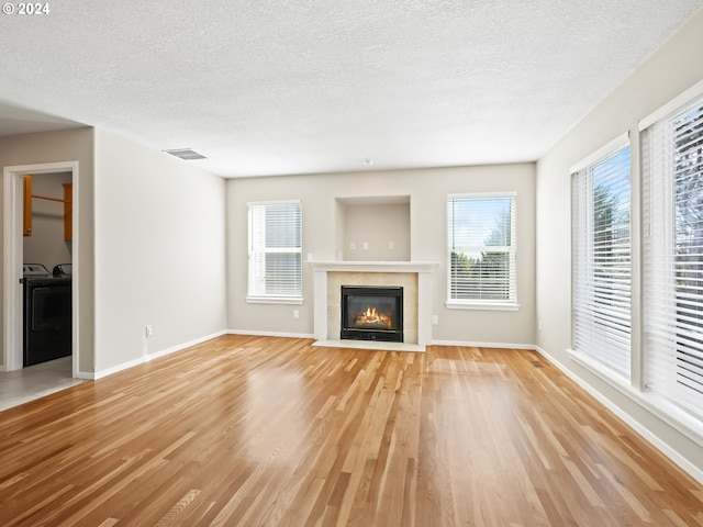 unfurnished living room featuring a tiled fireplace, separate washer and dryer, light hardwood / wood-style floors, and a textured ceiling