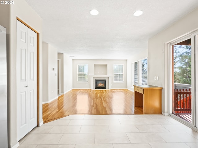 unfurnished living room with light tile patterned flooring, a healthy amount of sunlight, and a textured ceiling