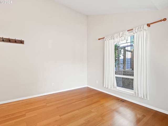 spare room featuring wood-type flooring and vaulted ceiling