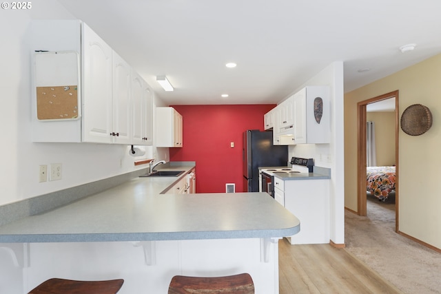 kitchen with a breakfast bar, a peninsula, electric range, freestanding refrigerator, and white cabinets