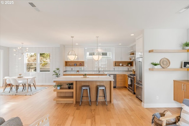 kitchen with light countertops, appliances with stainless steel finishes, open shelves, and light wood finished floors