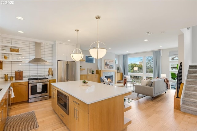 kitchen featuring light countertops, backsplash, stainless steel appliances, and wall chimney exhaust hood