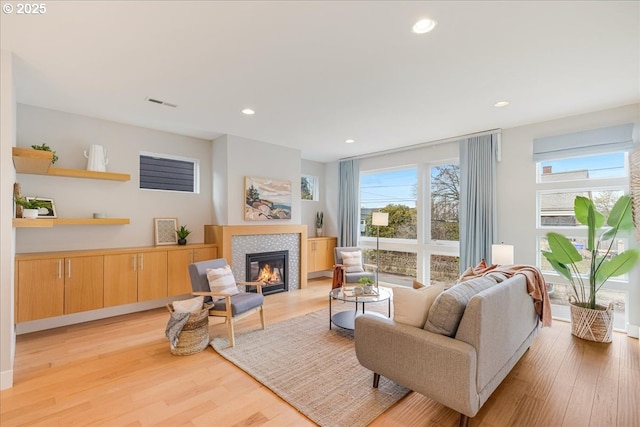 living room with recessed lighting, a tiled fireplace, a wealth of natural light, and light wood-type flooring