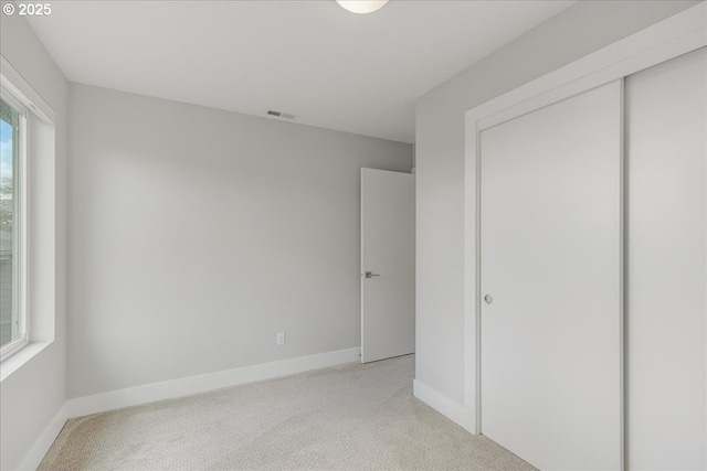 unfurnished bedroom featuring visible vents, baseboards, a closet, and light carpet