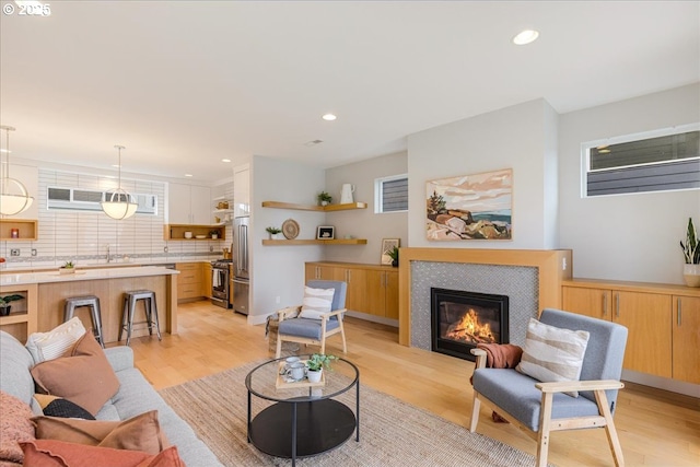 living room with recessed lighting, a tiled fireplace, and light wood-type flooring